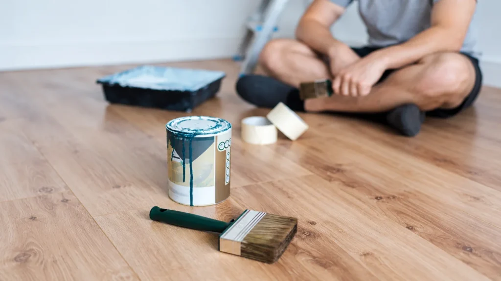 Bote de pintura goteando y brocha sobre un suelo de madera durante una reforma